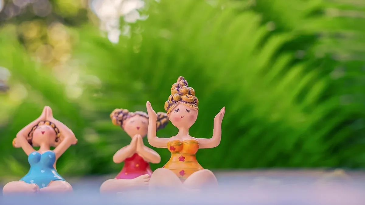 Three small figurines of women in yoga poses, with a blurred background of greenery.