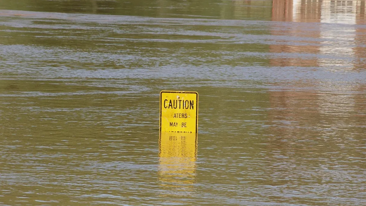 A yellow sign partially submerged in floodwaters, with a building visible in the background.