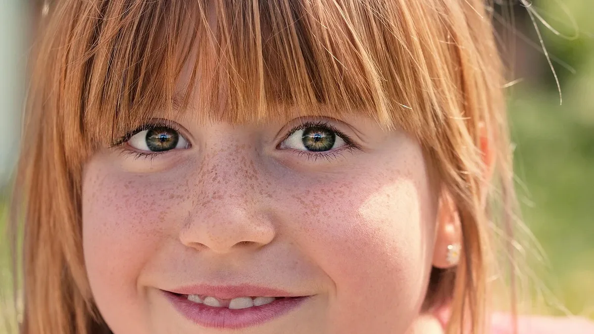A close-up of a young girl's face, with her hair, eyes, nose, mouth, and teeth visible.