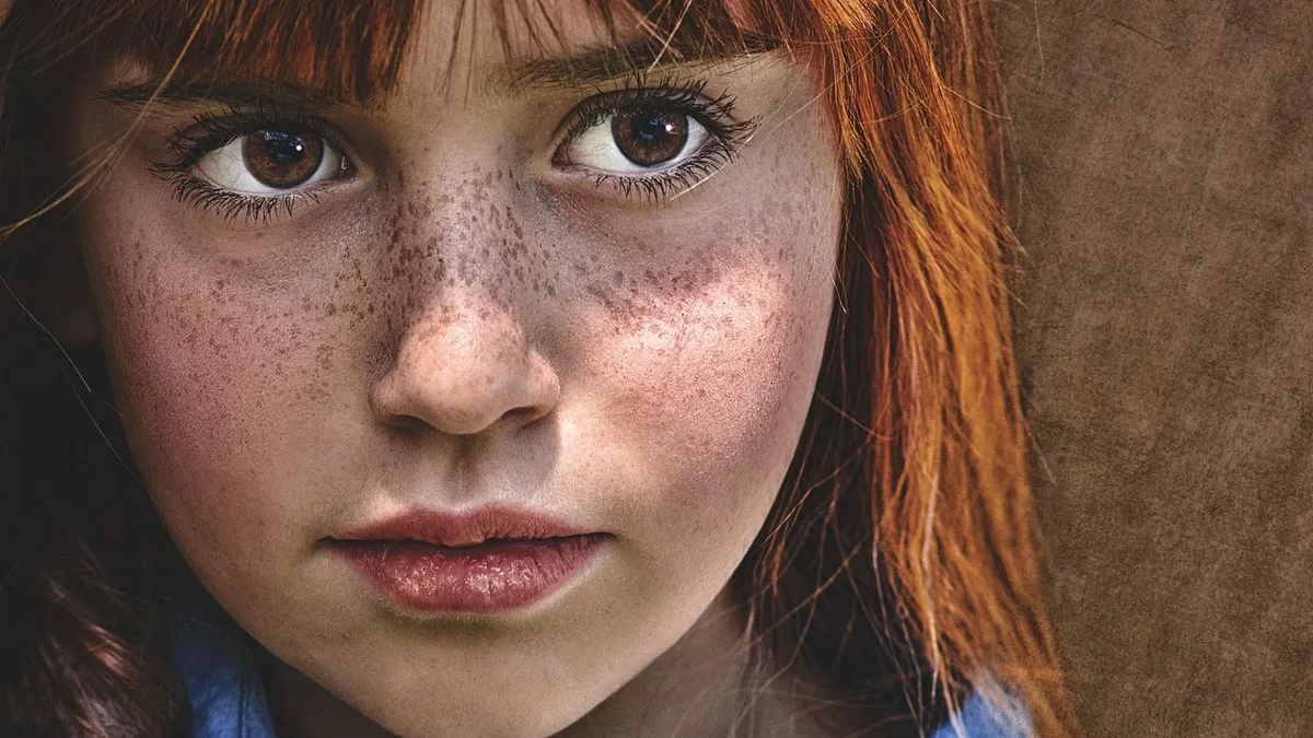 A close-up of a young girl's face, with her red hair and blue shirt visible.