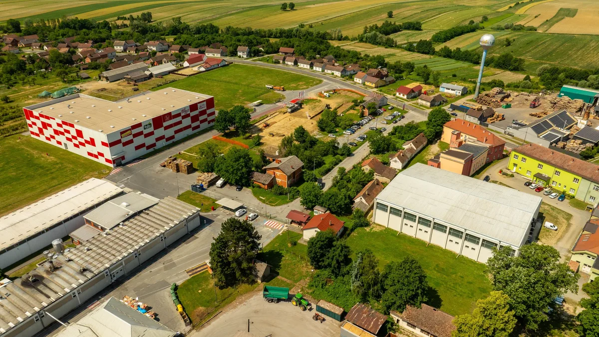 A small town or village with a mix of residential and industrial buildings, surrounded by fields and trees.